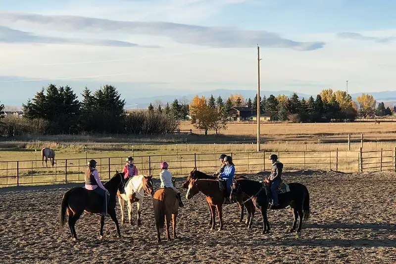 Students taking a horse riding lesson in an arena